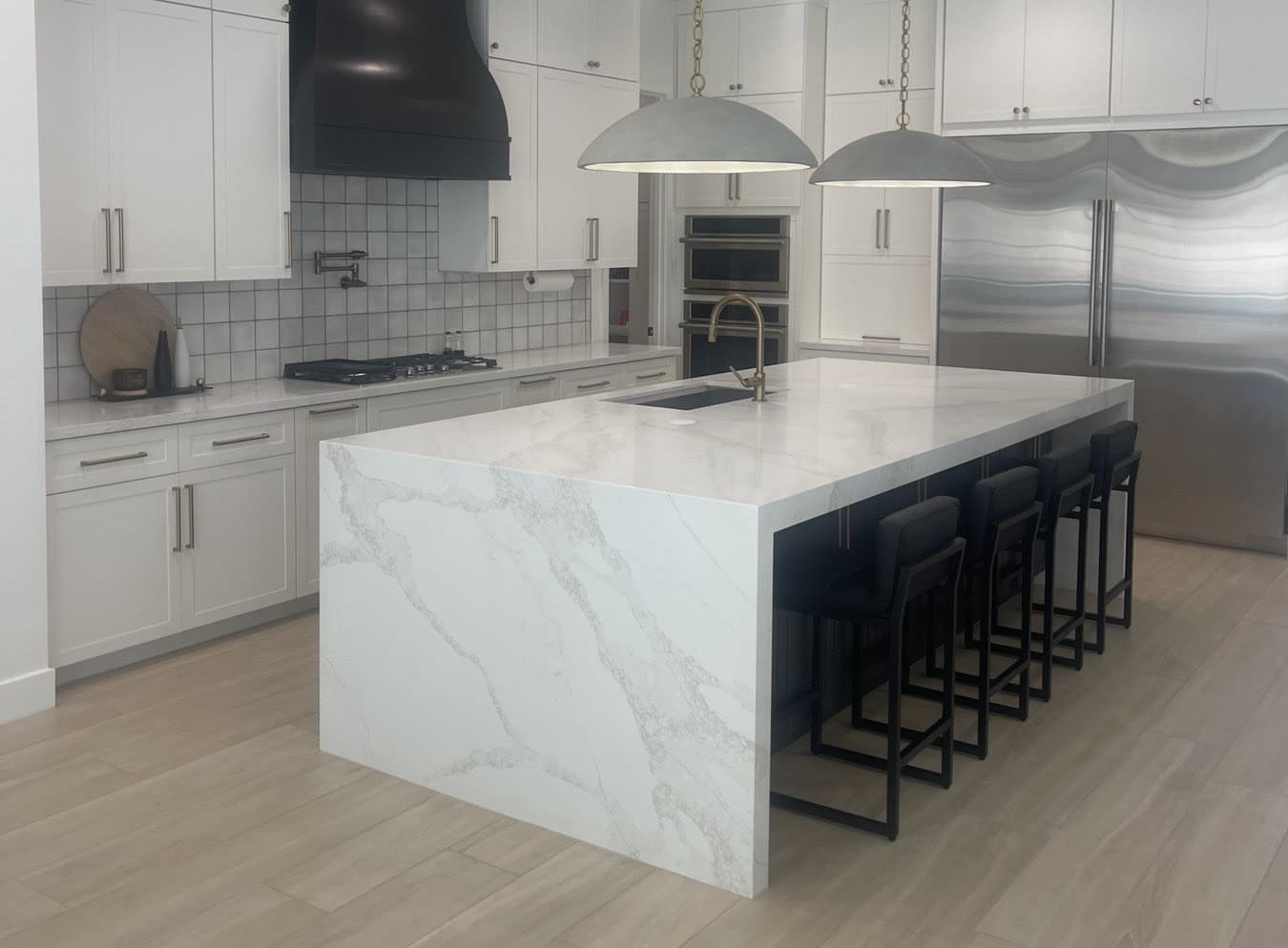 Bright white kitchen with a black range hood and a marble waterfall island in a Gilbert home