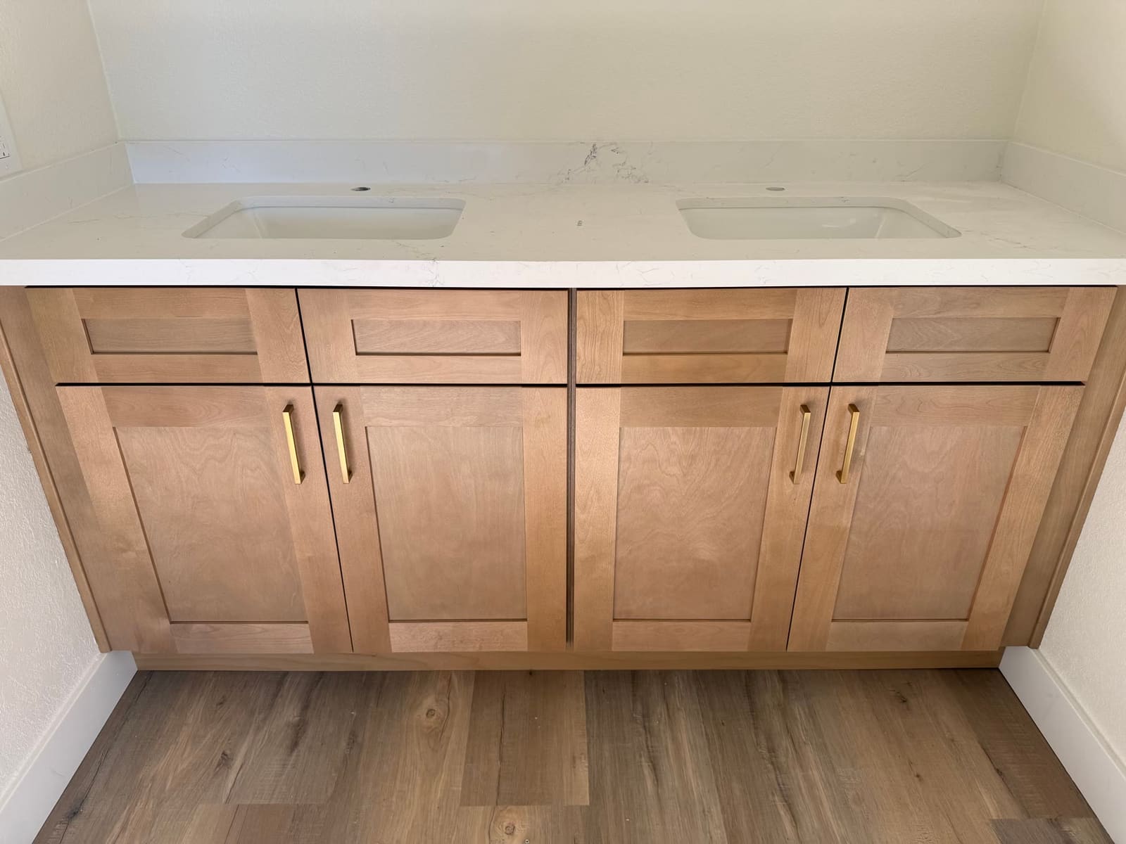 Natural-wood double-sink vanity with brushed-gold hardware and a quartz countertop