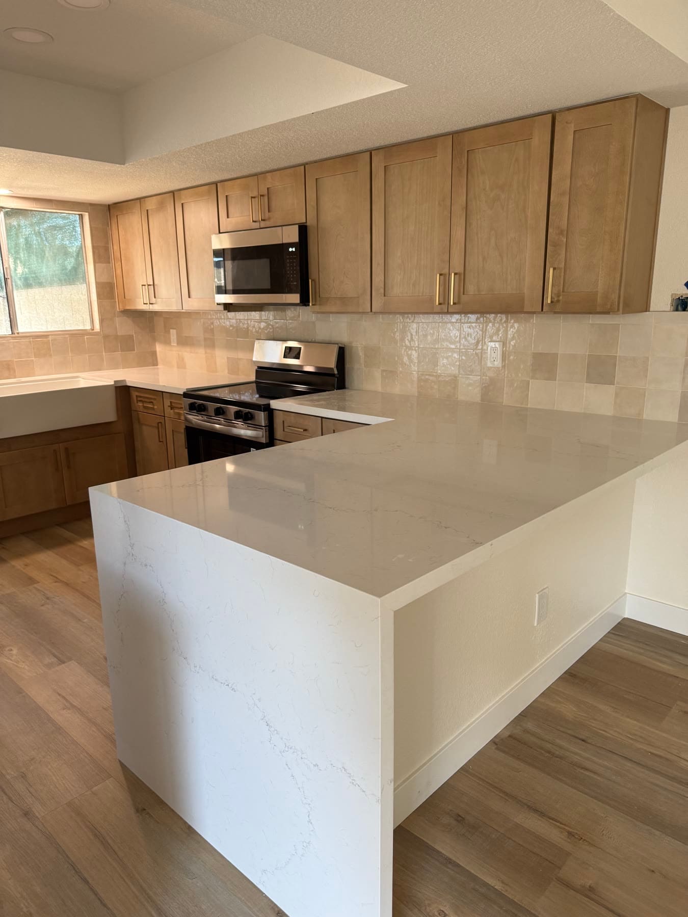 Natural-wood kitchen with a bright quartz waterfall peninsula and stainless appliances