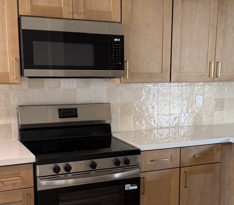 Handmade-look tile backsplash meeting natural-wood cabinetry behind a stainless range