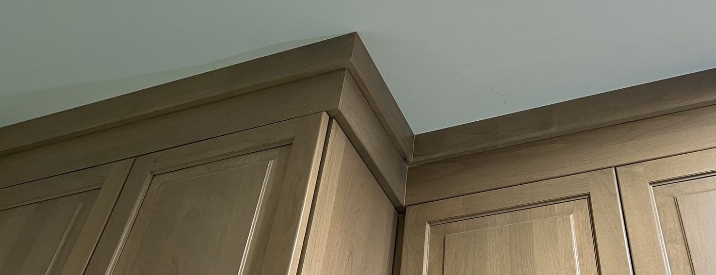 Crown molding run finishing the top of natural-wood wall cabinets