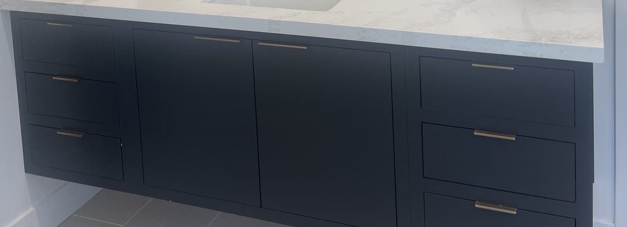 Drawer fronts of a floating navy vanity with slim brass pulls