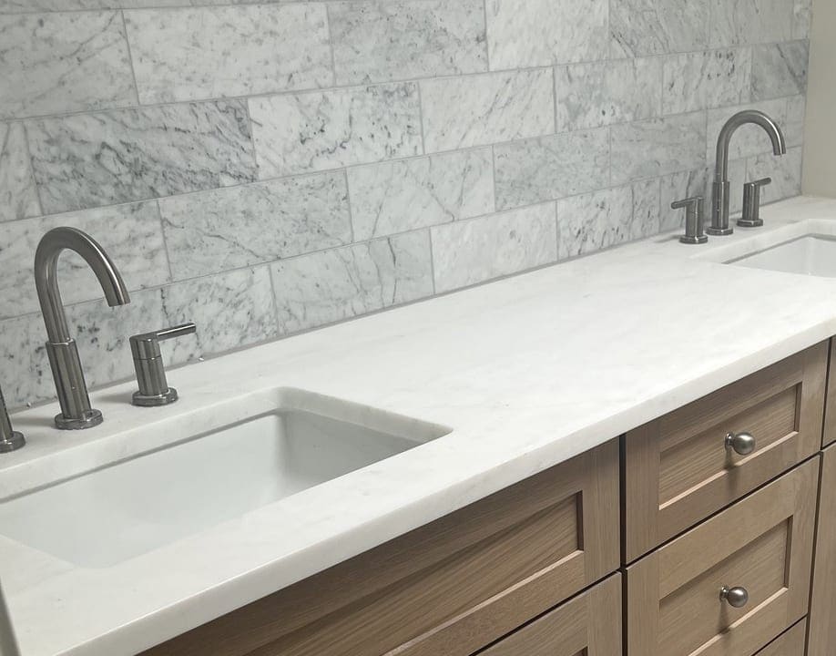 Marble subway backsplash meeting the quartz vanity top above an undermount sink