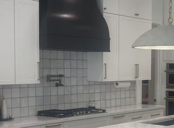 Black range hood above a white tile backsplash and gas cooktop