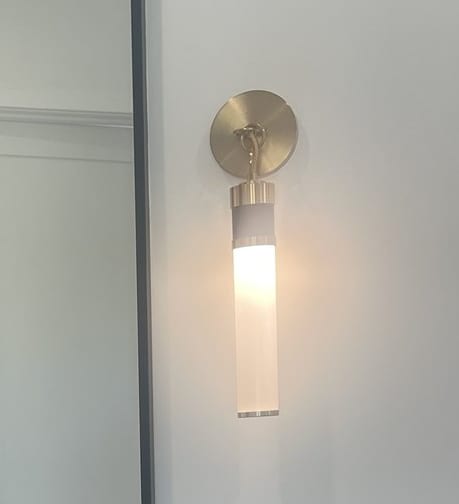 Brass wall sconce beside a black framed bathroom mirror